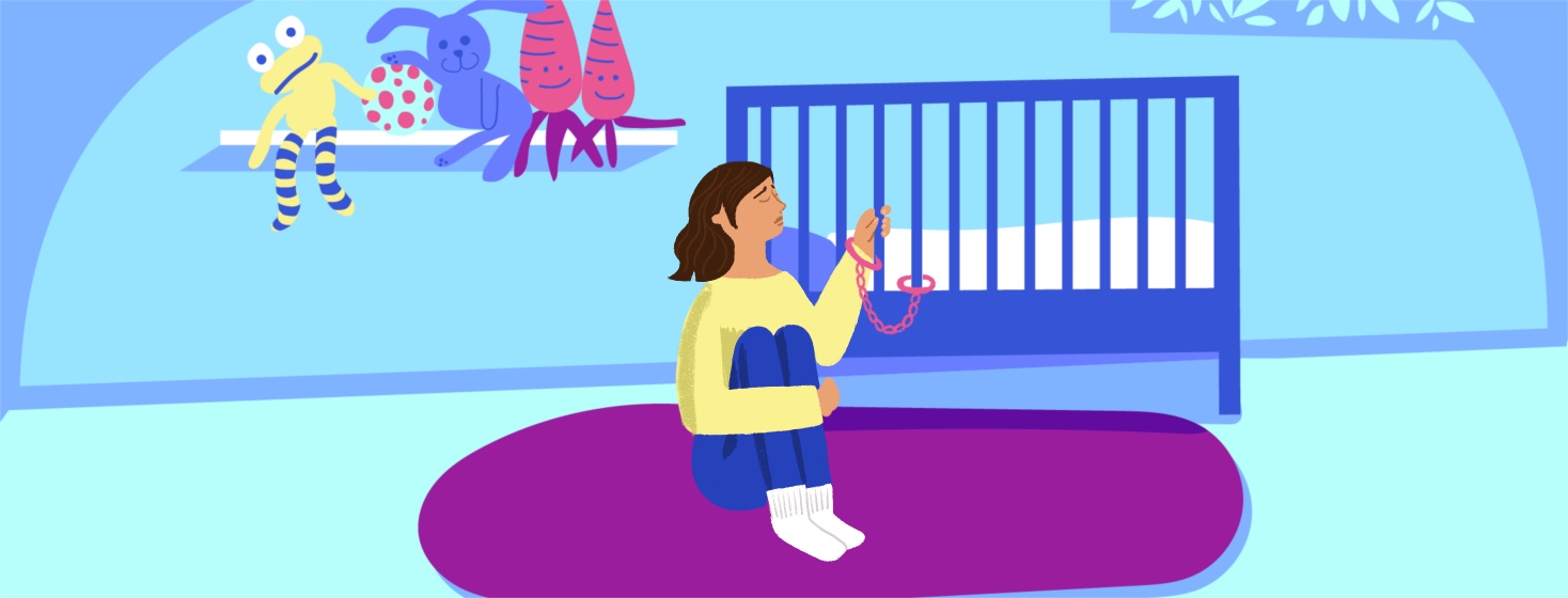 An anxious and sad woman is curled up next to her baby's crib, her wrist handcuffed to one of the bars